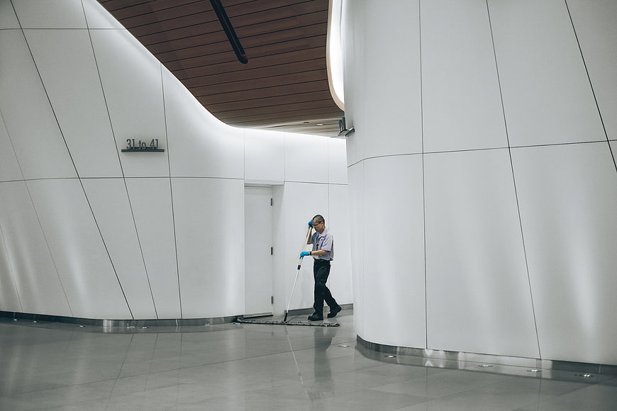 Janitor mopping floor in modern white curved hallway
