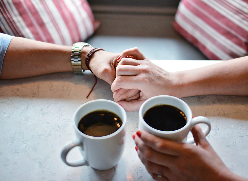 Couple holding hands over coffee cups in a cafe