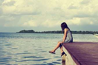 Woman sitting alone on wooden pier by calm sea