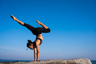 Woman performing advanced yoga handstand on coastal rock