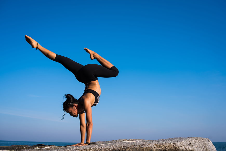 Woman performing advanced yoga handstand on coastal rock