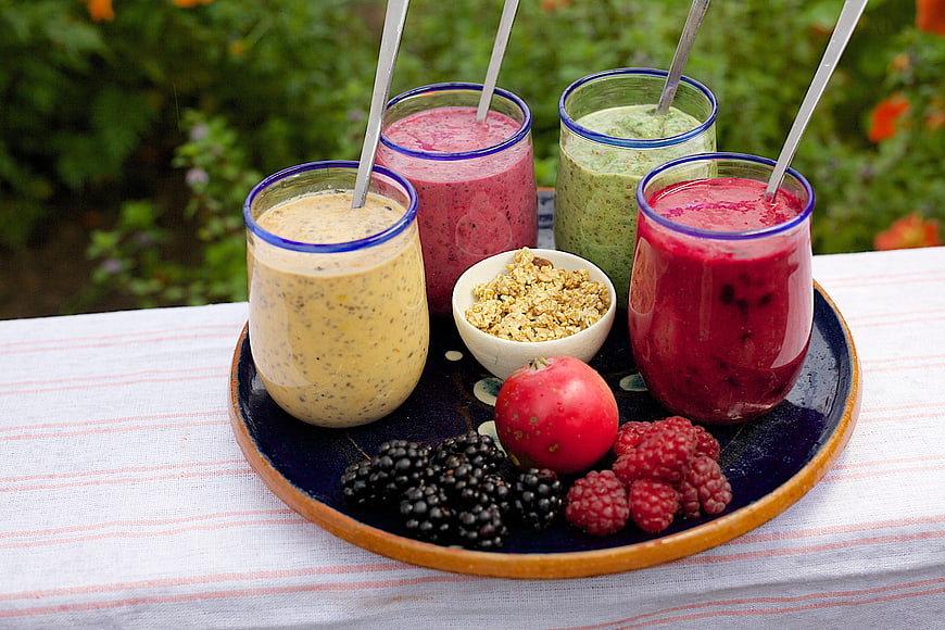 Colorful fruit smoothies with fresh berries and granola on a tray