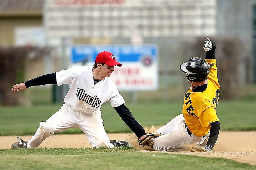 Baseball player sliding into base while fielder attempts tag