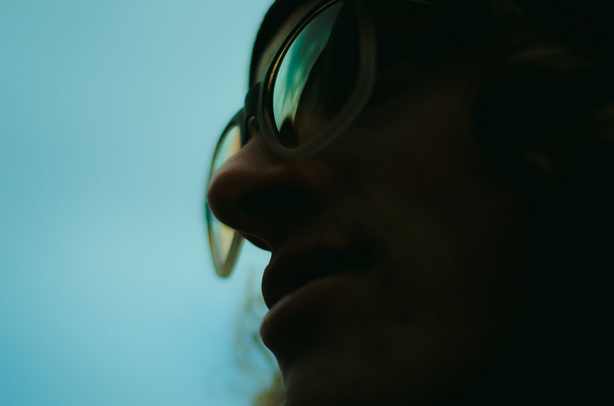Close-up profile of man wearing glasses against blue sky