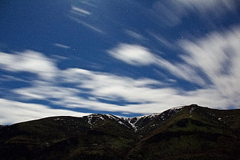 Dramatic Mountain Landscape with Streaking Clouds and Starry Sky