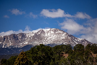 Snow-Capped Mountain Peak with Blue Sky and Foreground Trees