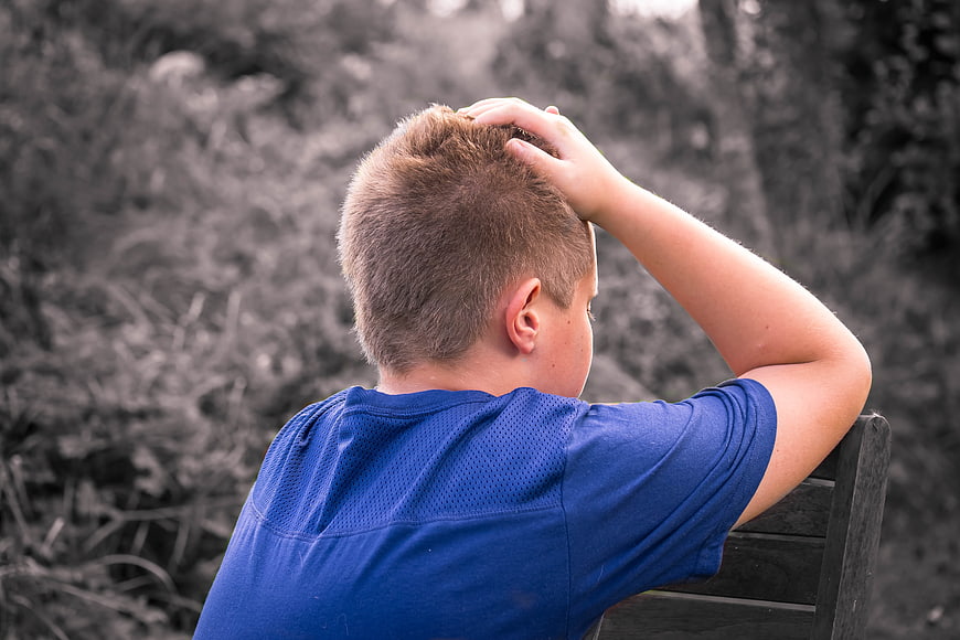 Sad Boy Sitting Alone on Bench with Hand on Head