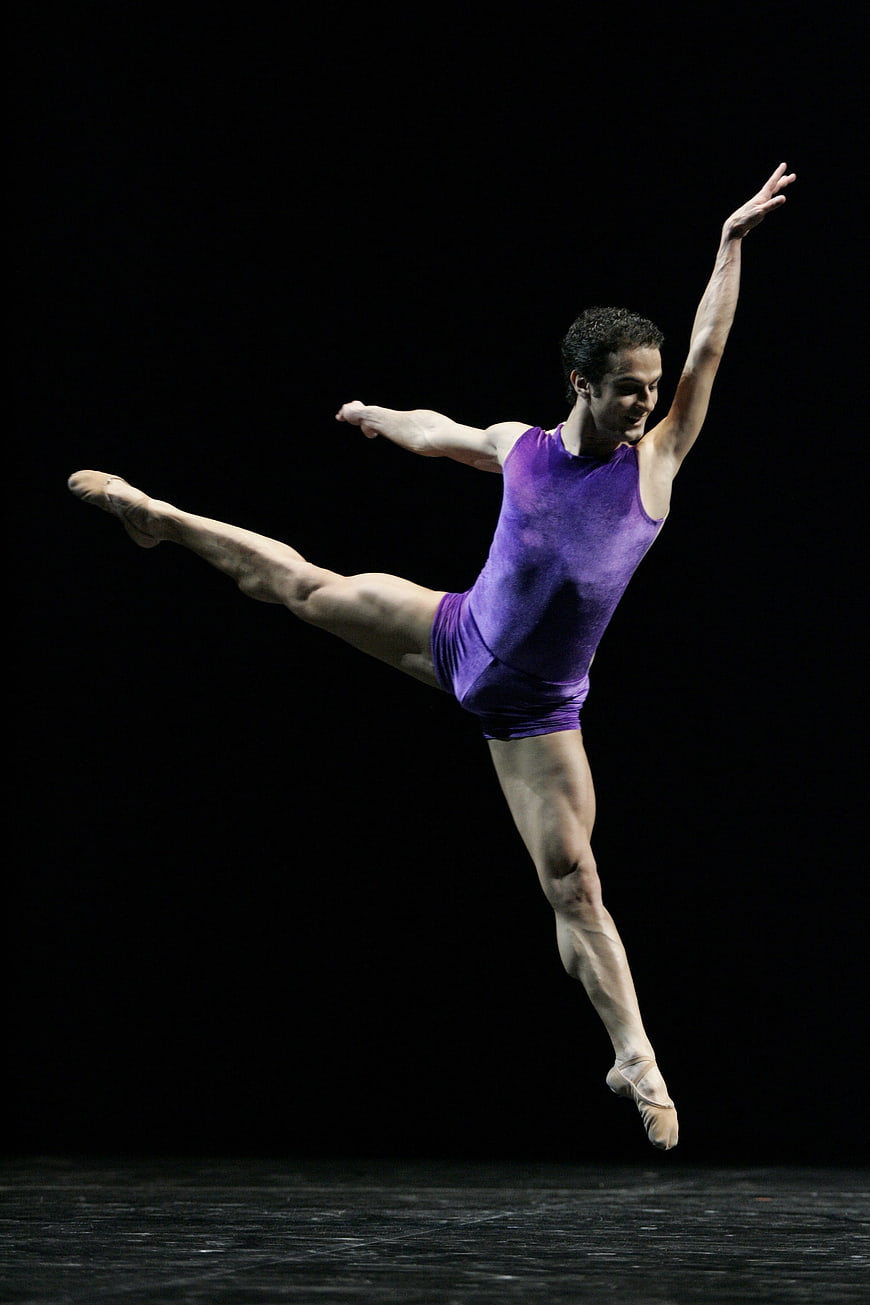 Male ballet dancer in purple leotard leaping mid-air