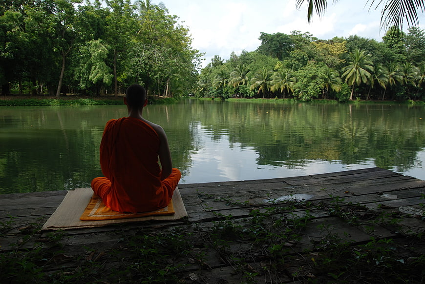 Buddhist monk meditating on a wooden dock by a serene tropical lake