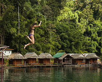 Woman Jumping into River Near Jungle Huts