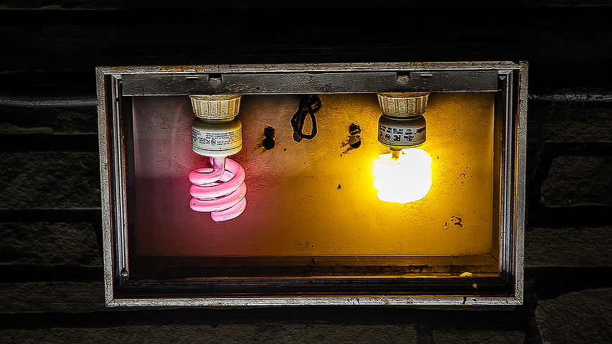 Two CFL light bulbs in a rusty metal box at night