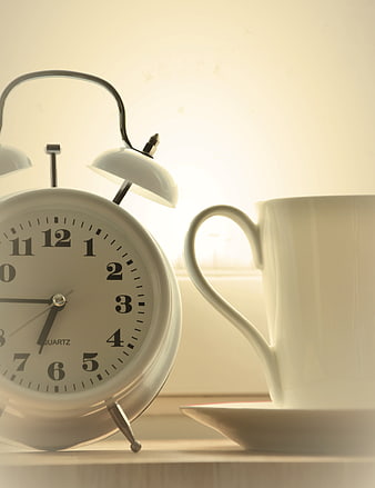 White alarm clock and coffee cup on windowsill with morning light