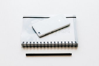 Minimalist white smartphone on spiral notebook with black pen