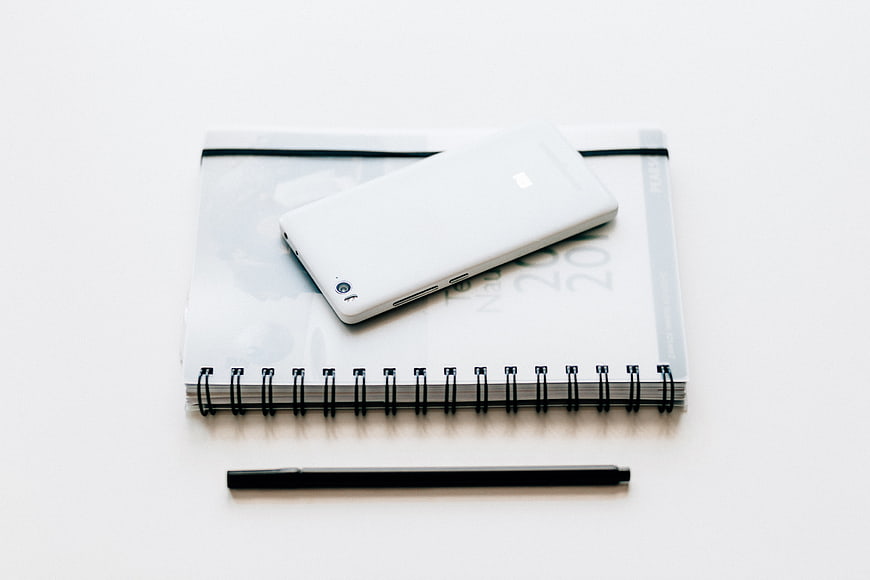 Minimalist white smartphone on spiral notebook with black pen