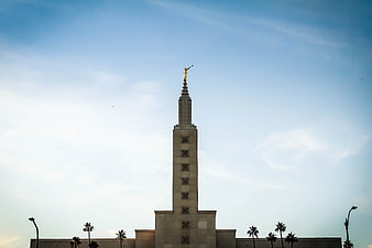 Tall Temple Spire with Golden Angel Statue Against Blue Sky