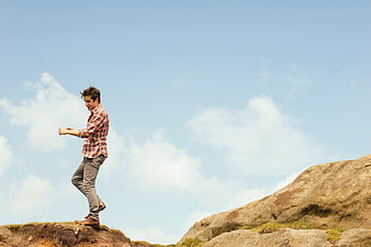 Young man standing on rocky cliff edge against blue sky
