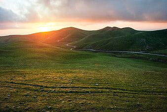 Winding Road Through Green Rolling Hills at Sunset