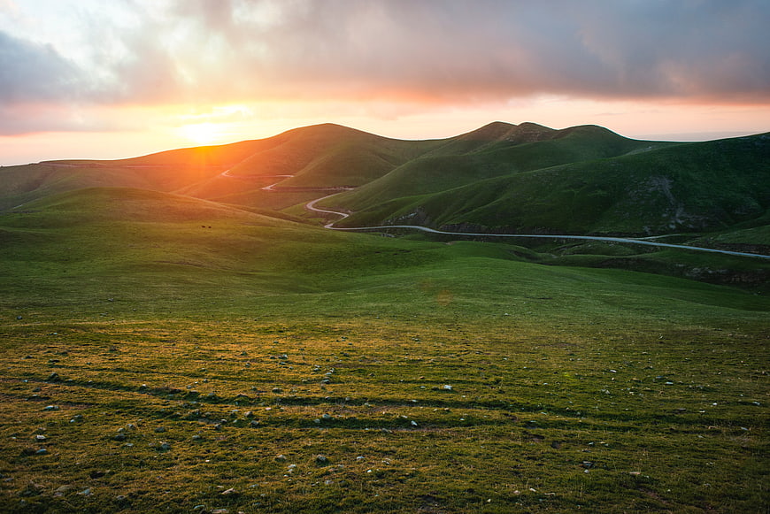 Winding Road Through Green Rolling Hills at Sunset
