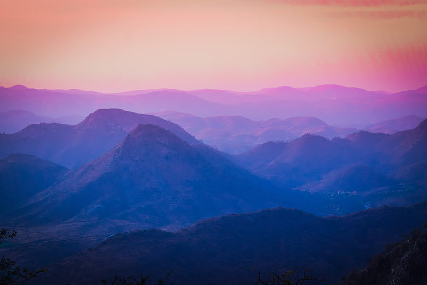 Layered mountain landscape at sunrise with pink and blue atmospheric haze