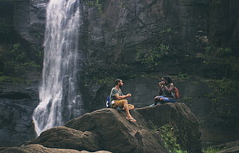 Couple relaxing on rocks by a scenic waterfall in nature