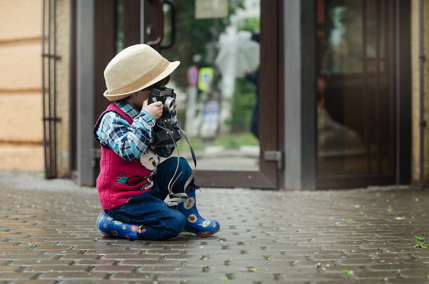 Toddler with vintage camera and straw hat on cobblestone street