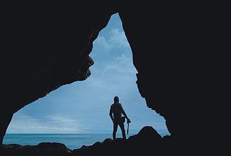 Silhouette of Man with Camera Looking Out from Cave to Ocean
