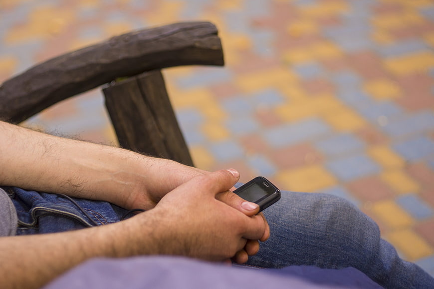 Man holding old mobile phone on park bench