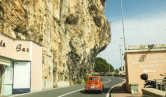 Vintage orange car driving along coastal cliff road