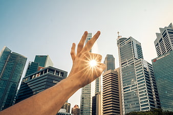 Hand Reaching For Sunlight Against City Skyline