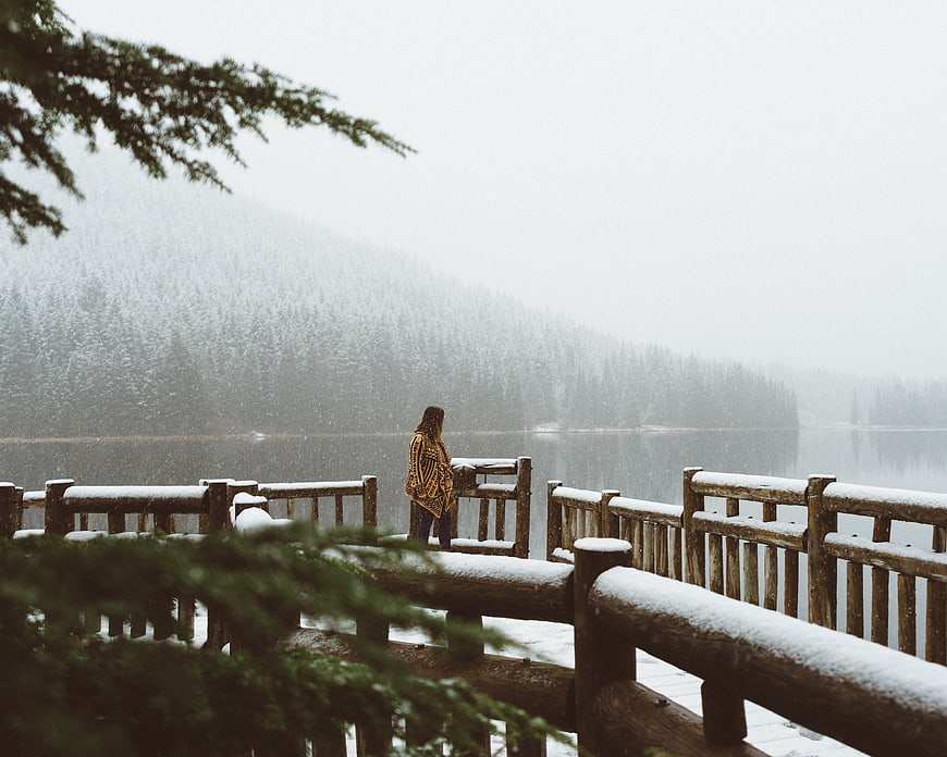 Woman standing on snowy wooden pier overlooking misty lake