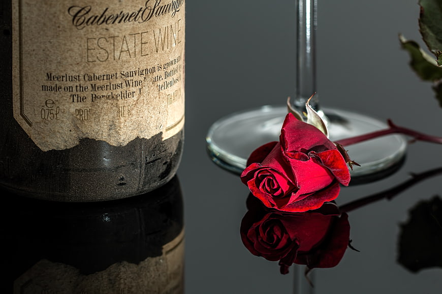 Vintage wine bottle and red rose on reflective surface