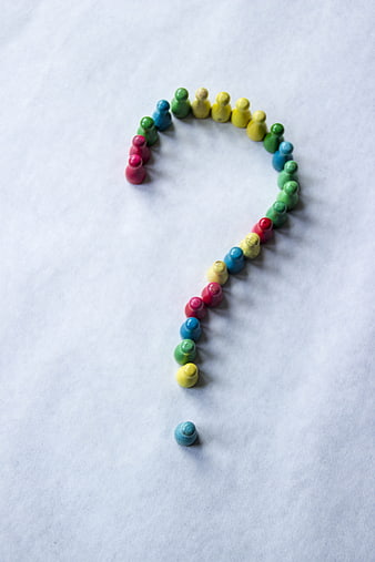 Colorful wooden pegs arranged in a question mark shape on white paper