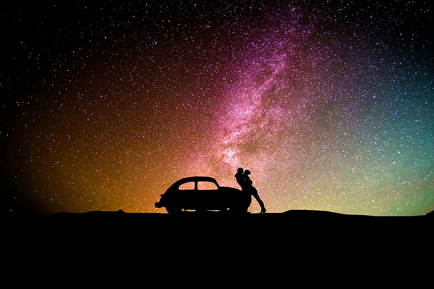 Silhouette of couple and car under vibrant Milky Way night sky