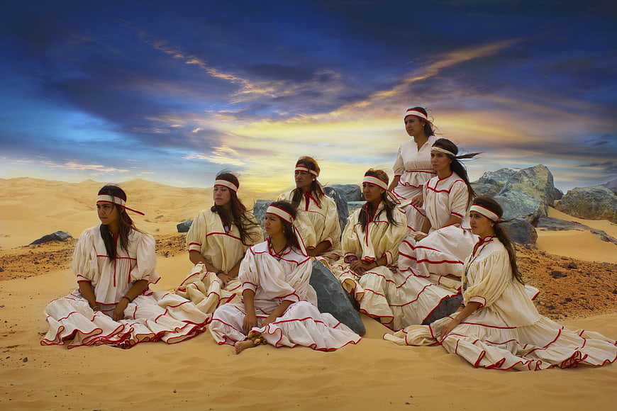 Group of Indigenous Women in Traditional Dress Seated in Desert Landscape