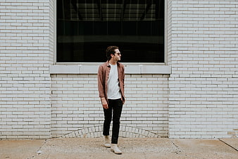 Man in Rust Jacket Standing Against White Brick Wall