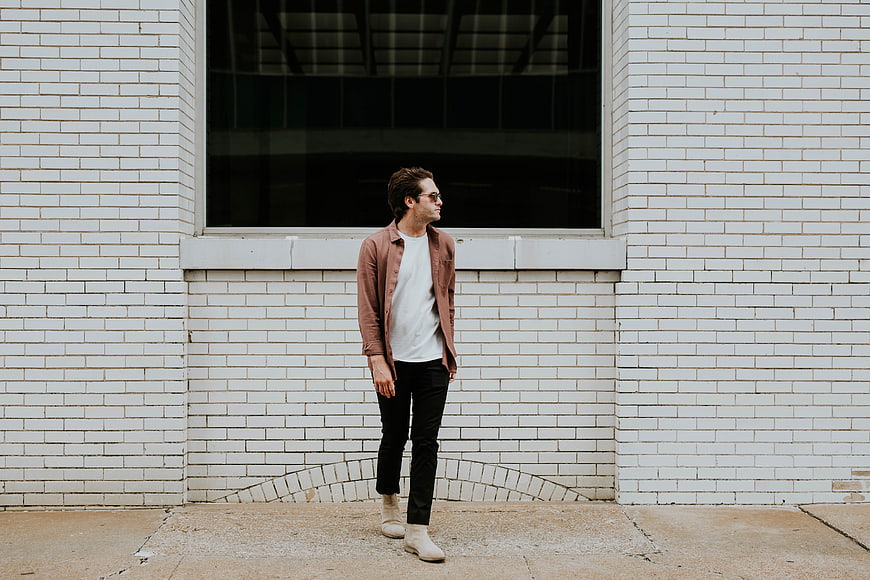 Man in Rust Jacket Standing Against White Brick Wall