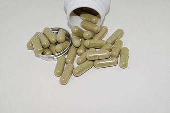 Green herbal supplement capsules spilling from white bottle and metal tin