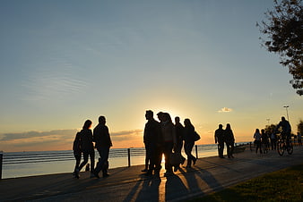 Silhouettes of people walking along seaside promenade at sunset