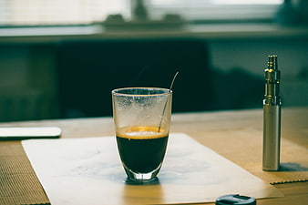 Half-empty espresso glass and vape pen on wooden table