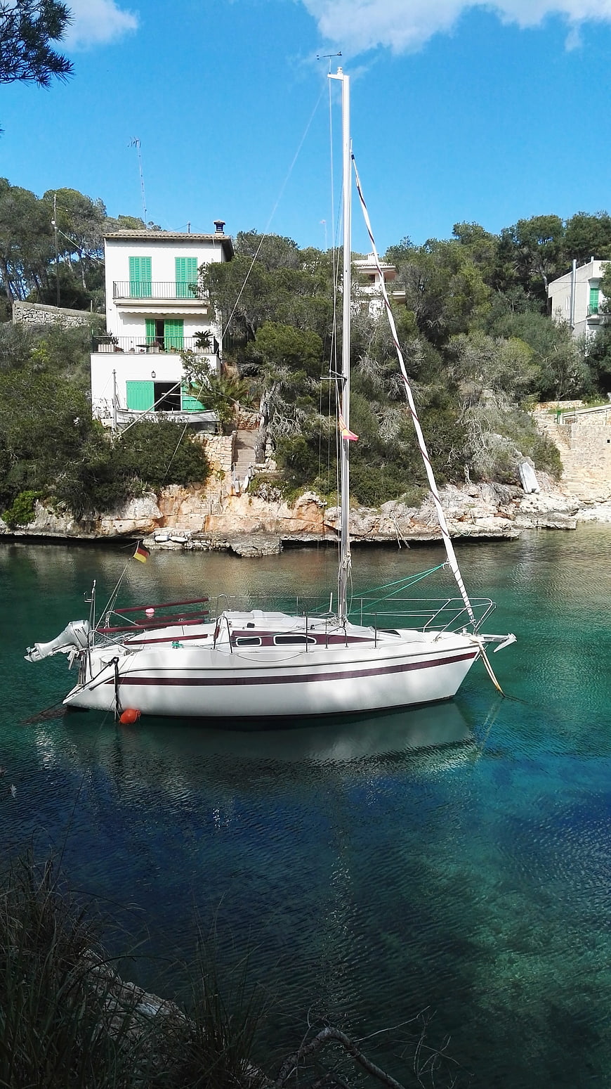 White sailboat anchored in turquoise Mediterranean cove