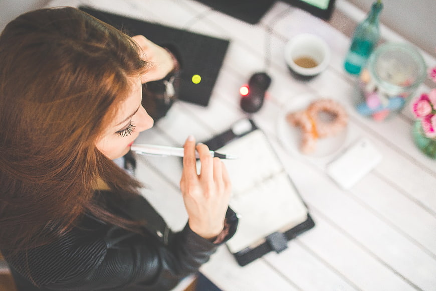 Young woman thinking with pen at white desk