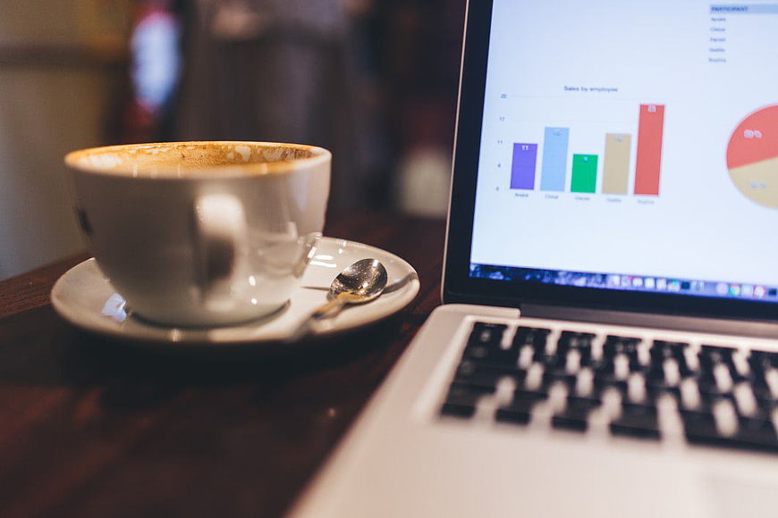 Laptop with business charts and coffee cup on wooden table