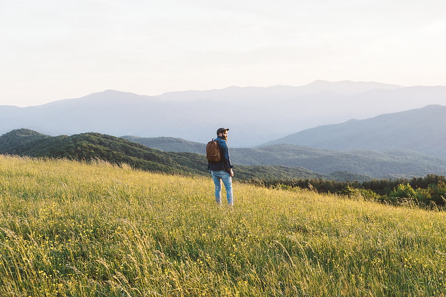 Man Hiking in Grassy Mountain Field with Backpack