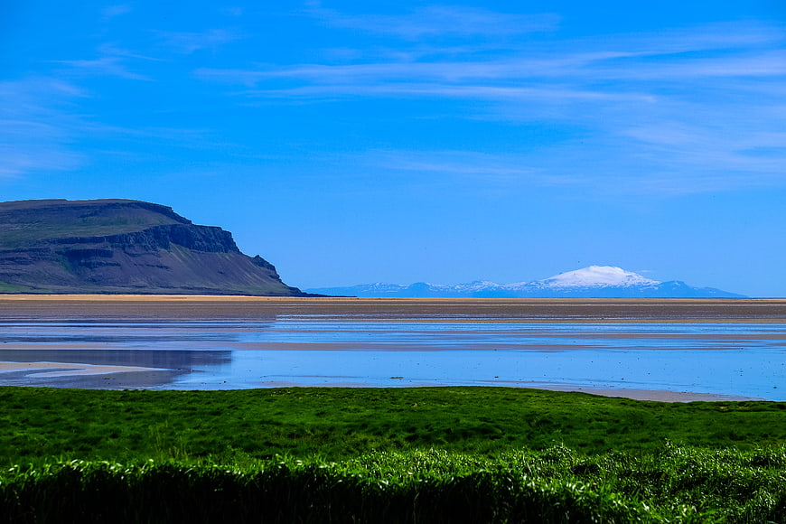 Scenic Icelandic Landscape with Green Grass, Blue Sky, and Distant Snowy Mountain