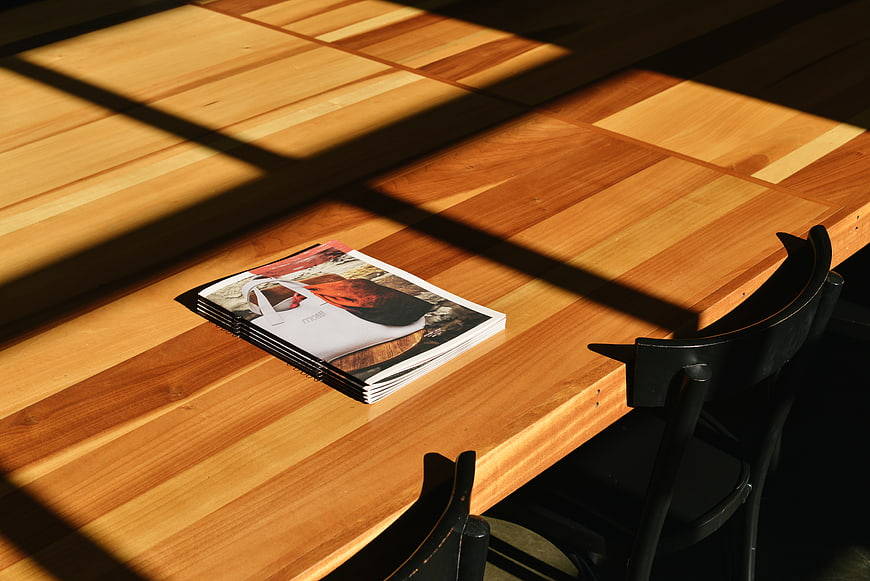 Stack of magazines on wooden table with sunlight shadows