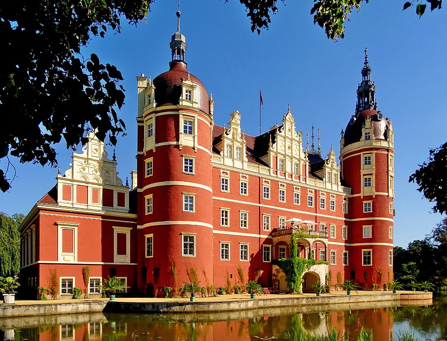 Red and white baroque castle with towers near water