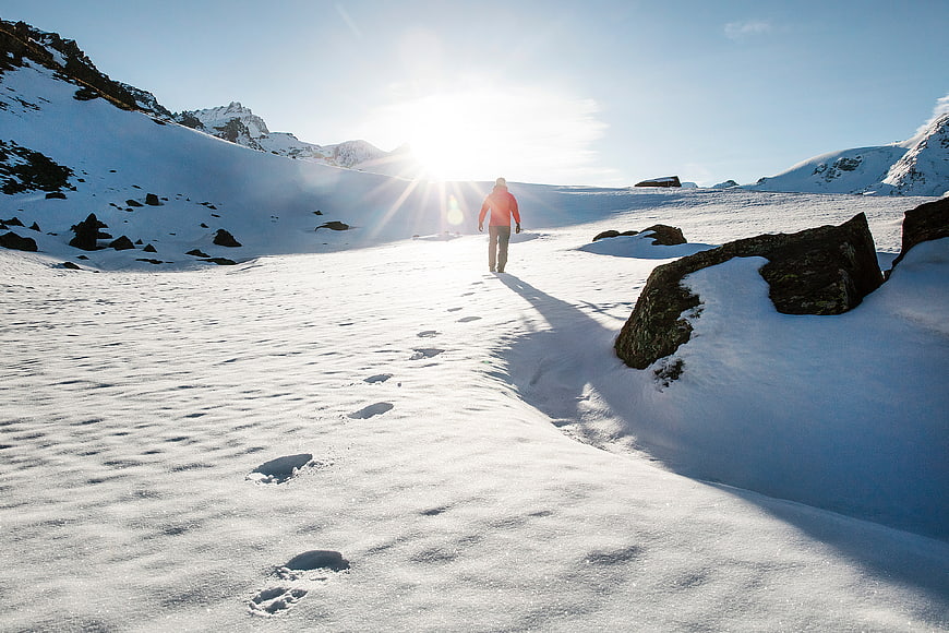 Lone Hiker Walking in Snowy Mountain Landscape with Sunlight