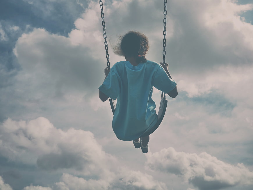 Child on Swing Against Cloudy Sky