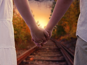 Couple Holding Hands on Railway Tracks at Sunset