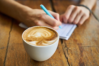 Cappuccino with Latte Art on Wooden Table with Person Writing